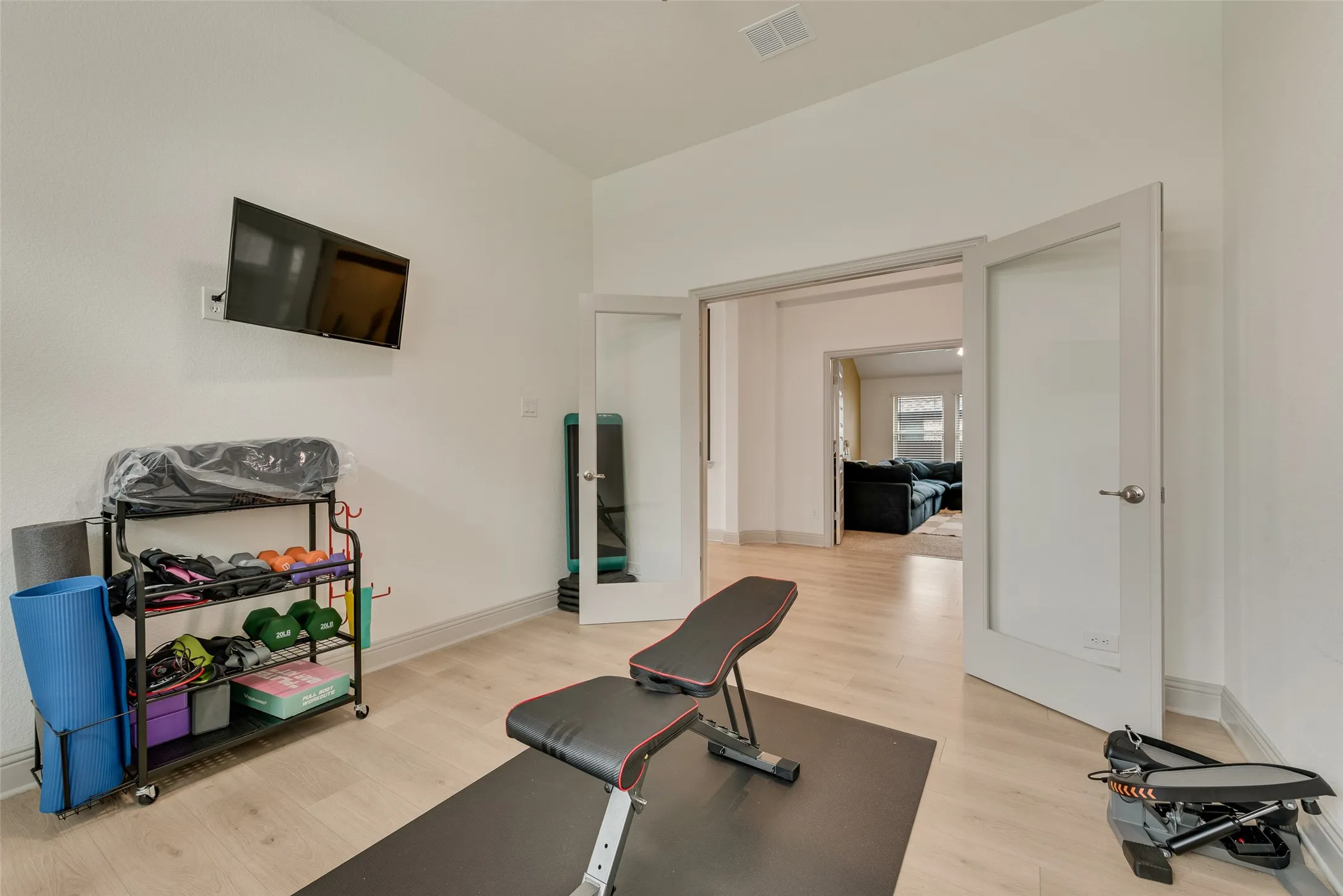Enclosed study currently used as an exercise room, with double doors and wood-finish flooring