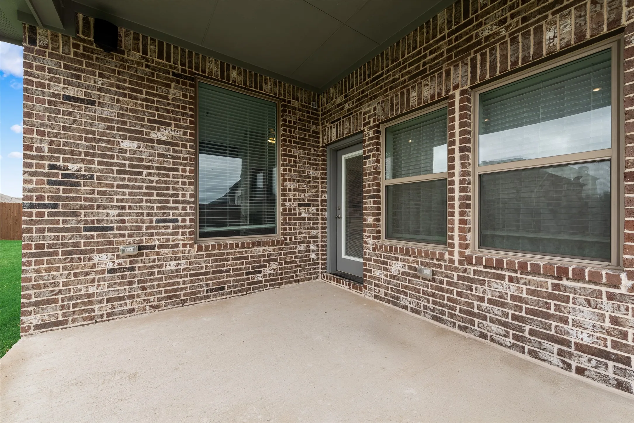 Covered patio featuring brick exterior, concrete flooring, and multiple windows