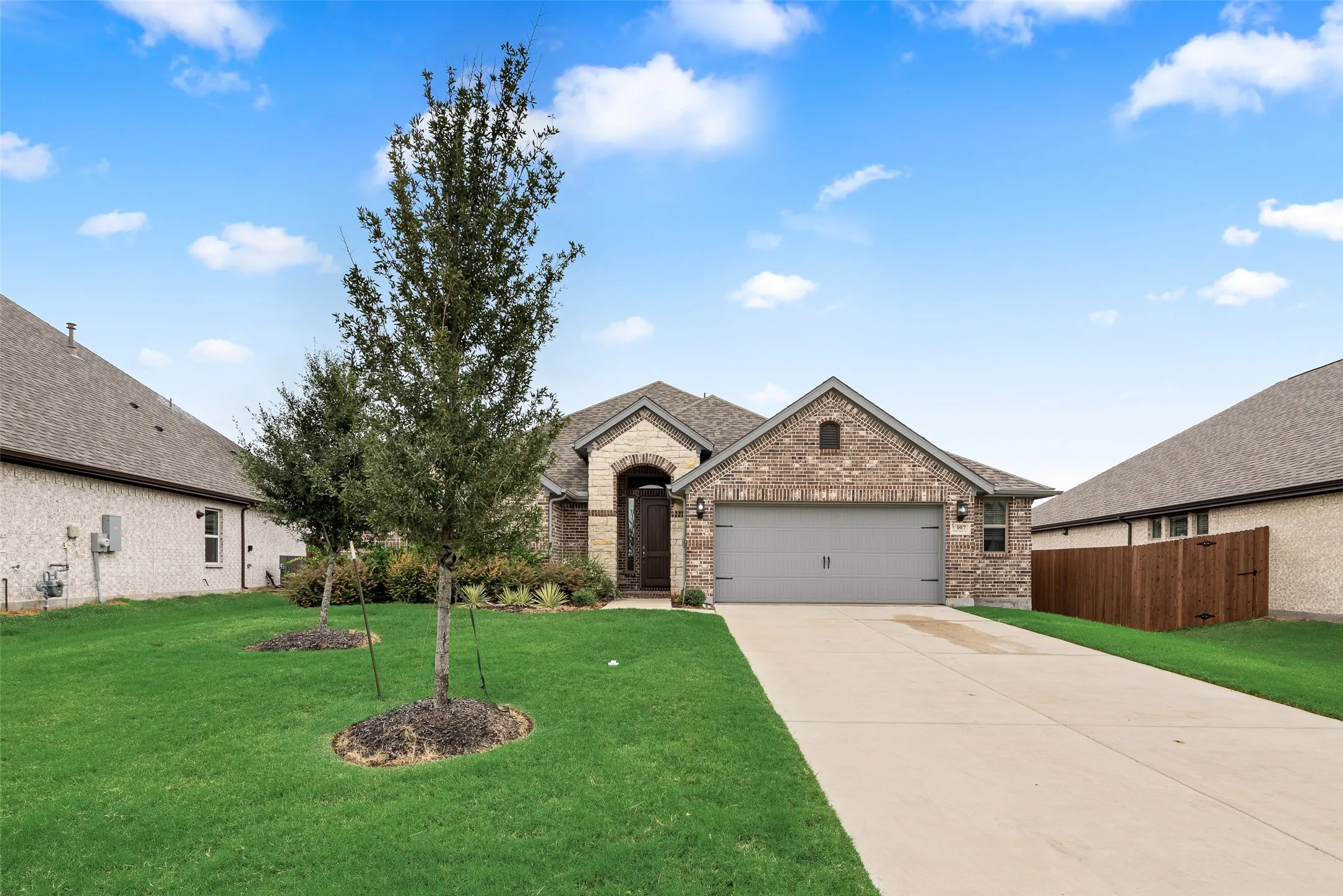 Brick facade with a covered entry, attached garage with a carriage-style door, concrete driveway, and manicured lawn