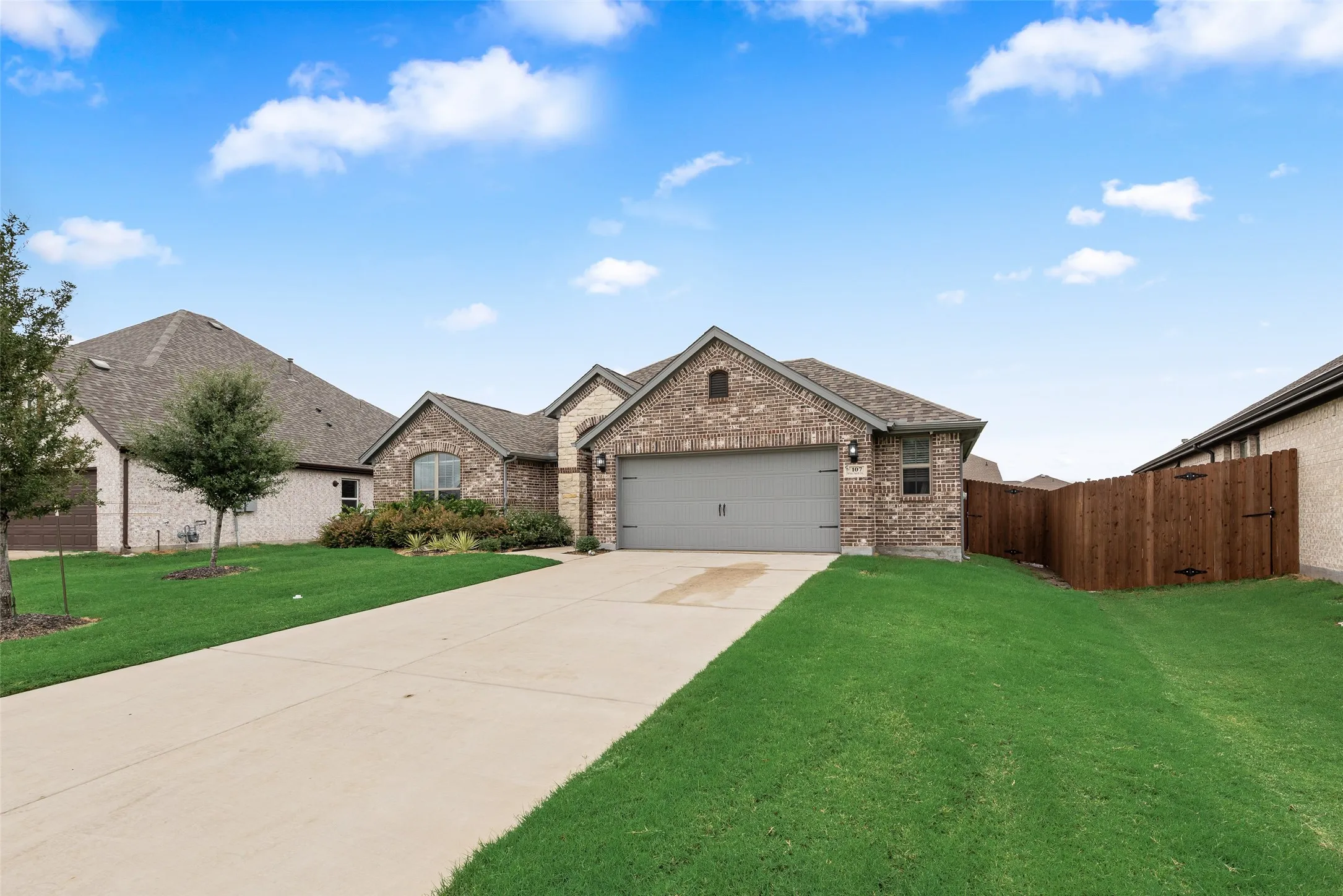 Brick exterior, attached garage, concrete driveway, front landscaping, and wood privacy fence