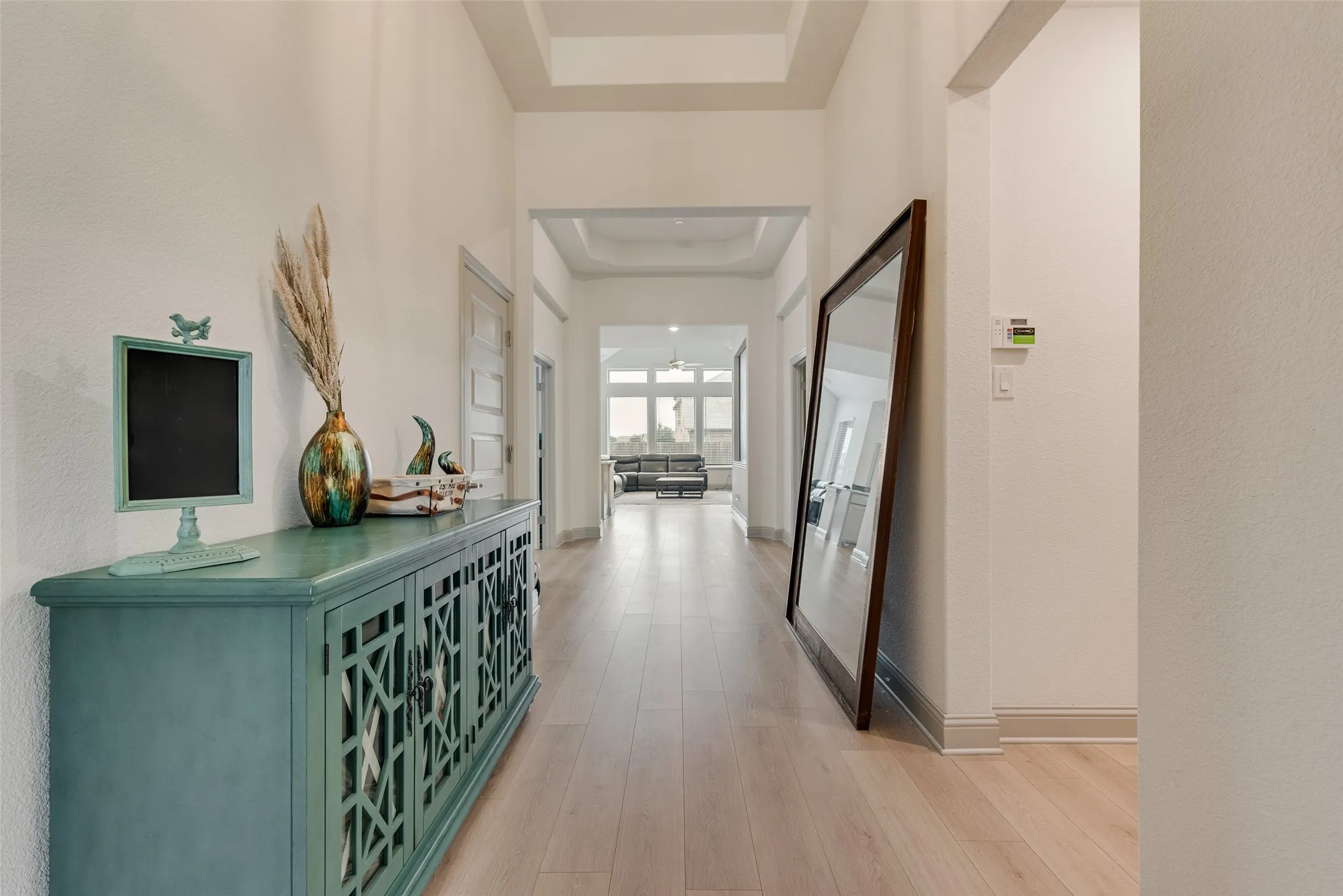 Long hallway with wood-finish flooring, tray ceiling, and neutral wall tones