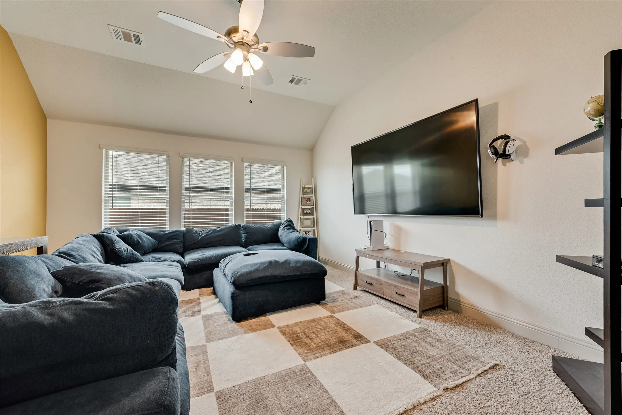 Separate game room with a ceiling fan, three windows with blinds, and carpeted flooring