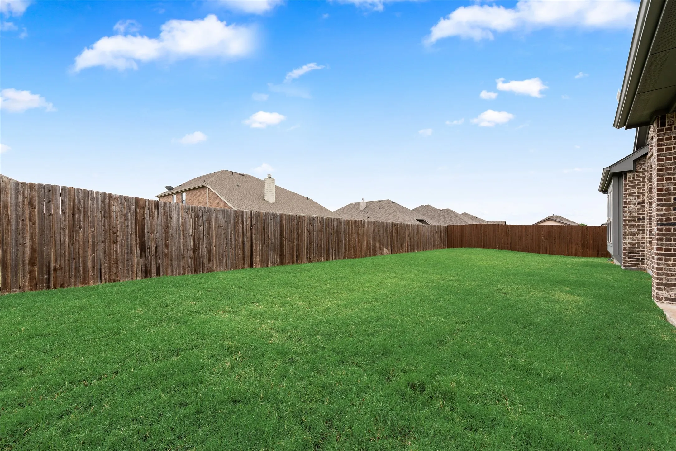 Expansive grassy yard area with a wood privacy fence and brick exterior