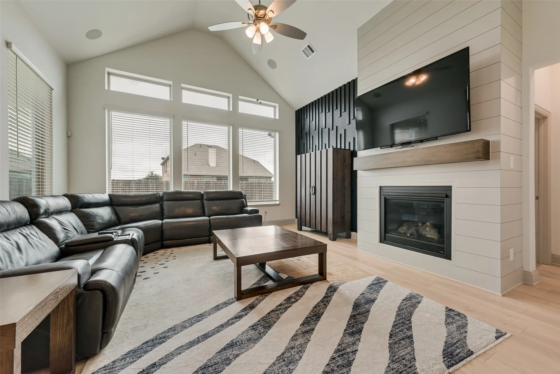 Vaulted ceiling with a ceiling fan, fireplace with a wood mantel, wood-finish flooring, and expansive windows