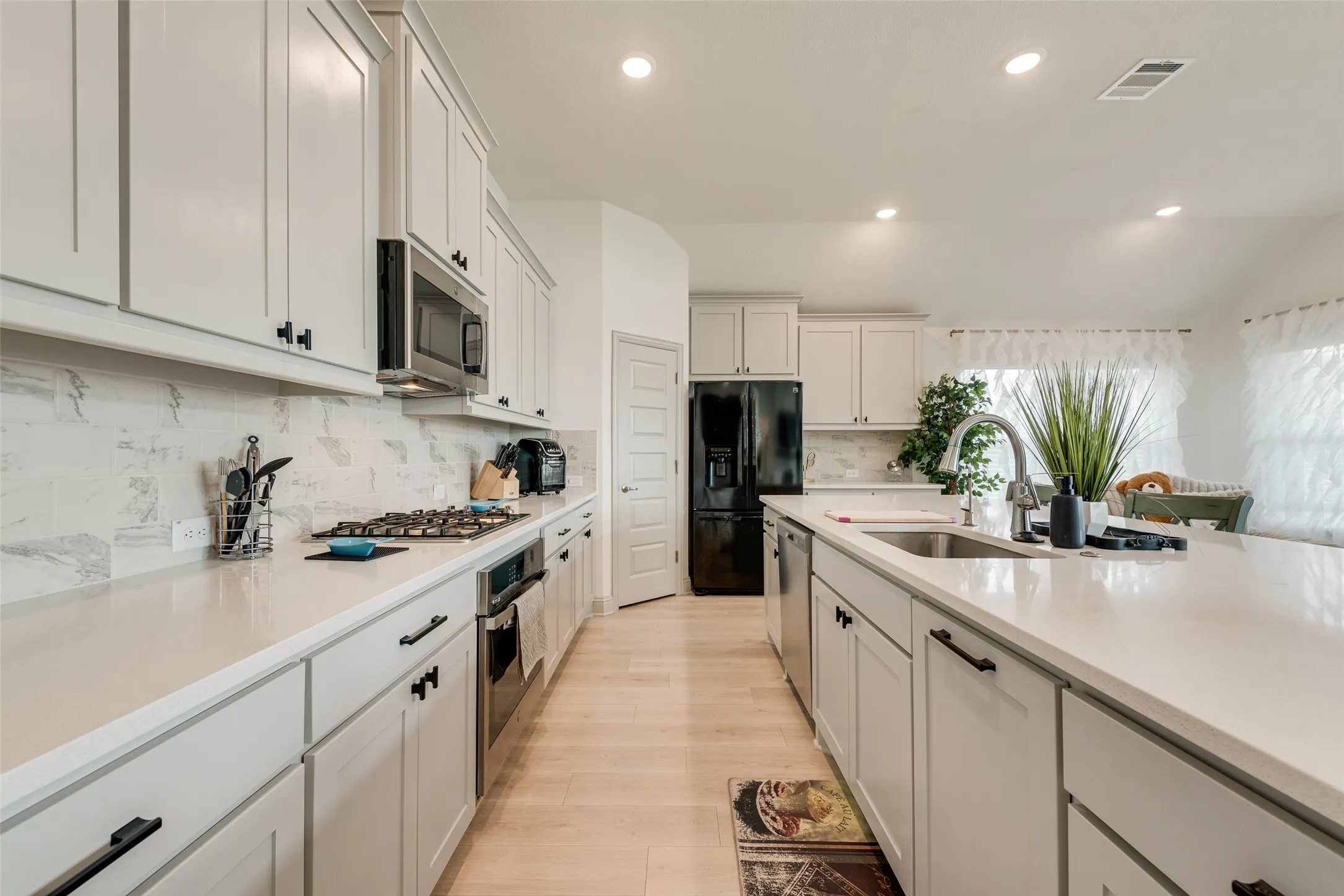 Kitchen featuring extensive light-toned cabinetry with matte black hardware, integrated stainless steel appliances, light-toned countertops, and a full-height tile backsplash