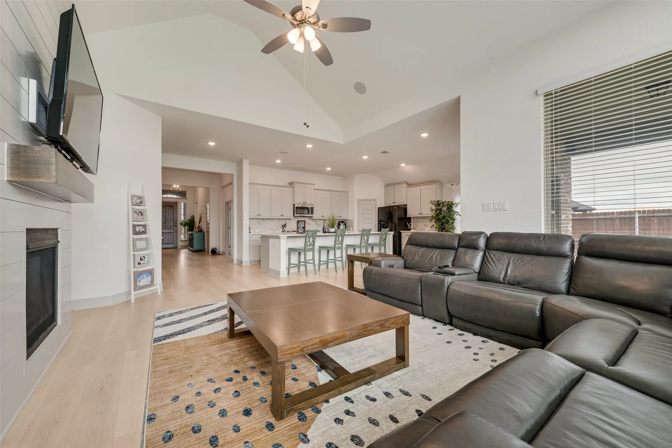 Vaulted ceiling with a ceiling fan, light wood-finish flooring, and a fireplace with shiplap-style surround and wood mantel