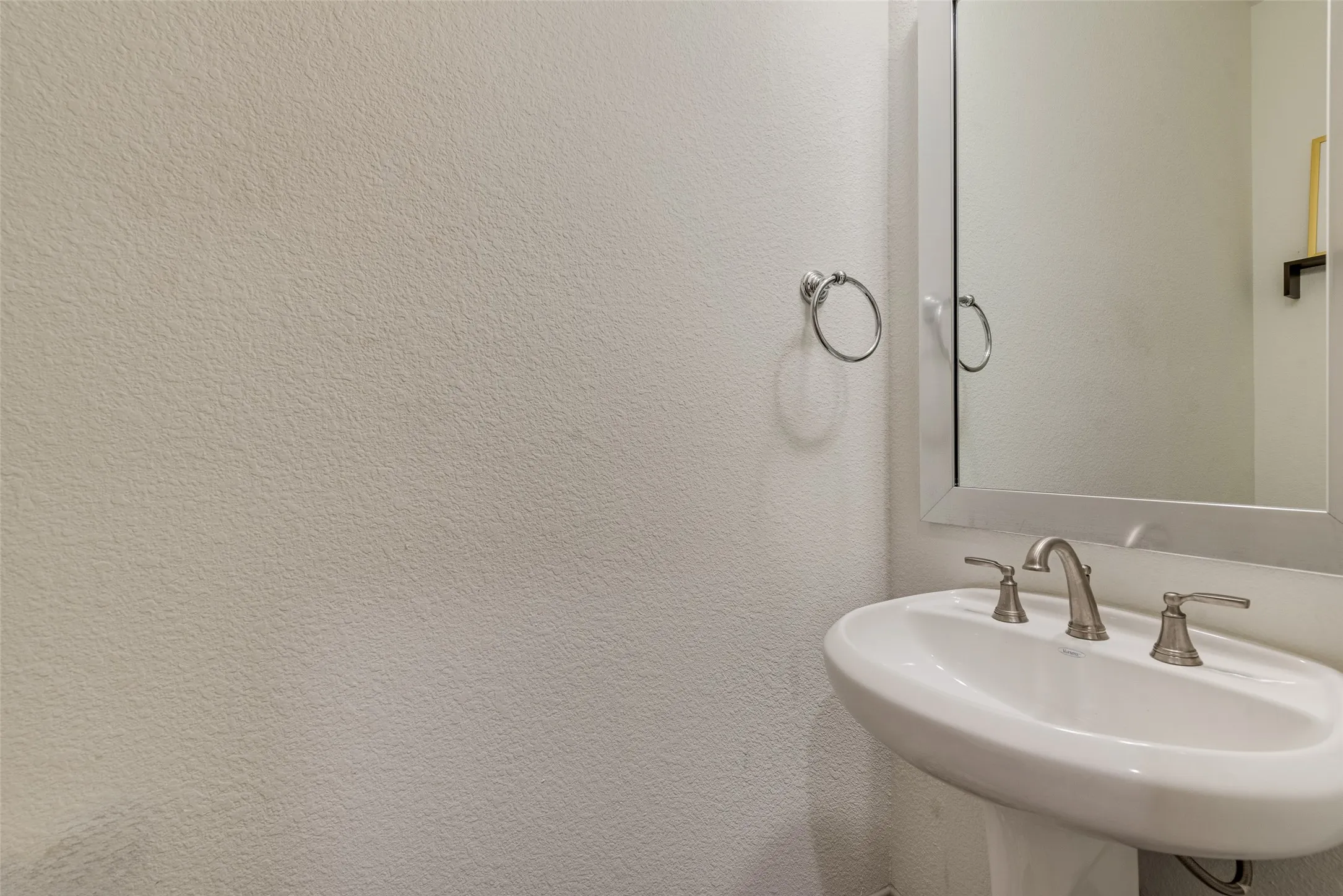 Half bathroom with a pedestal sink, two-handle faucet, and wall mirror