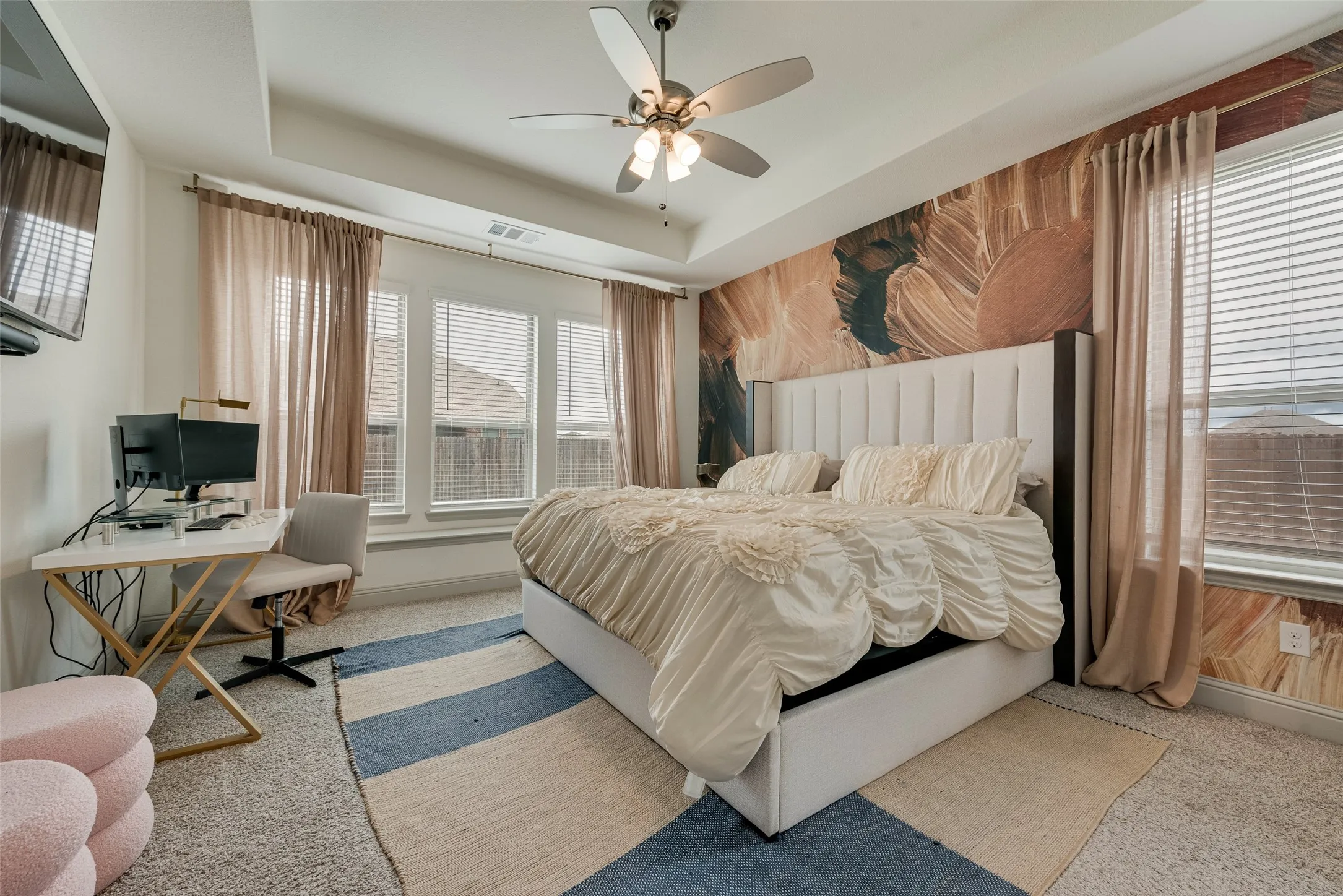 Primary bedroom with a tray ceiling, ceiling fan, multiple large windows, and carpeted flooring