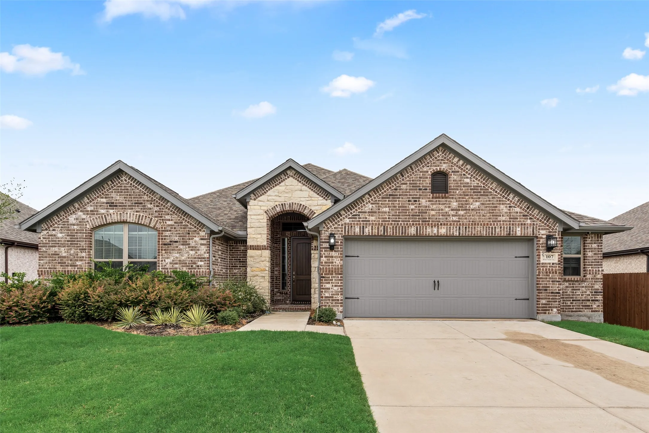 Brick exterior with an arched entryway, attached two-car garage, and established landscaping