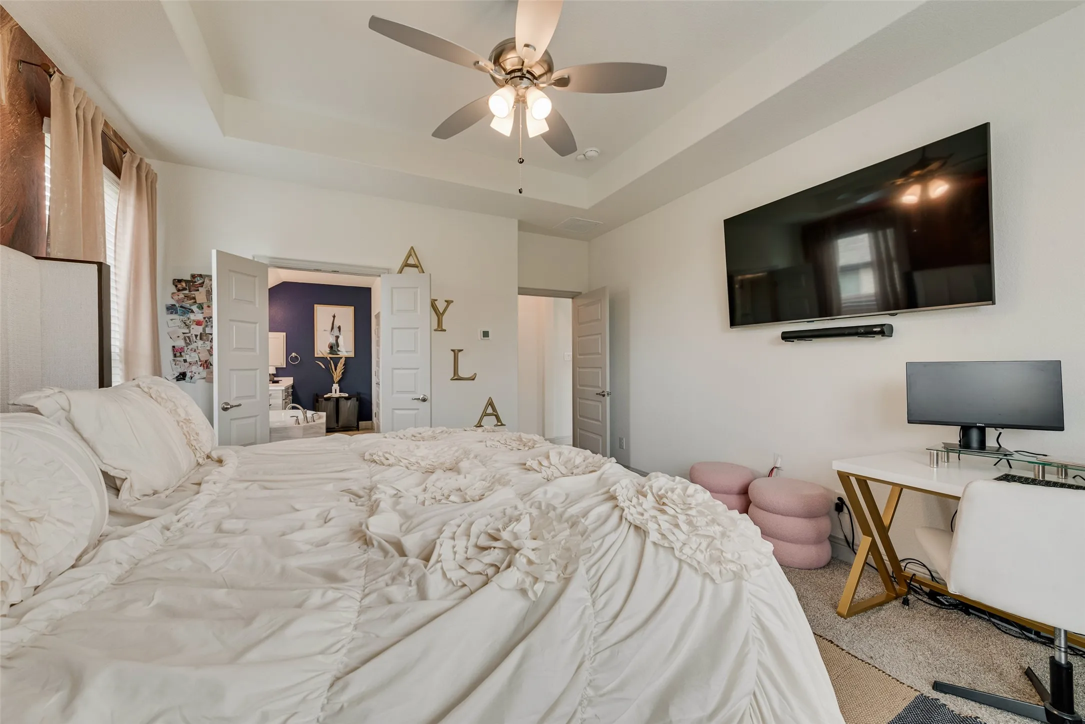 Primary bedroom with a tray ceiling and ceiling fan; view toward the ensuite bathroom