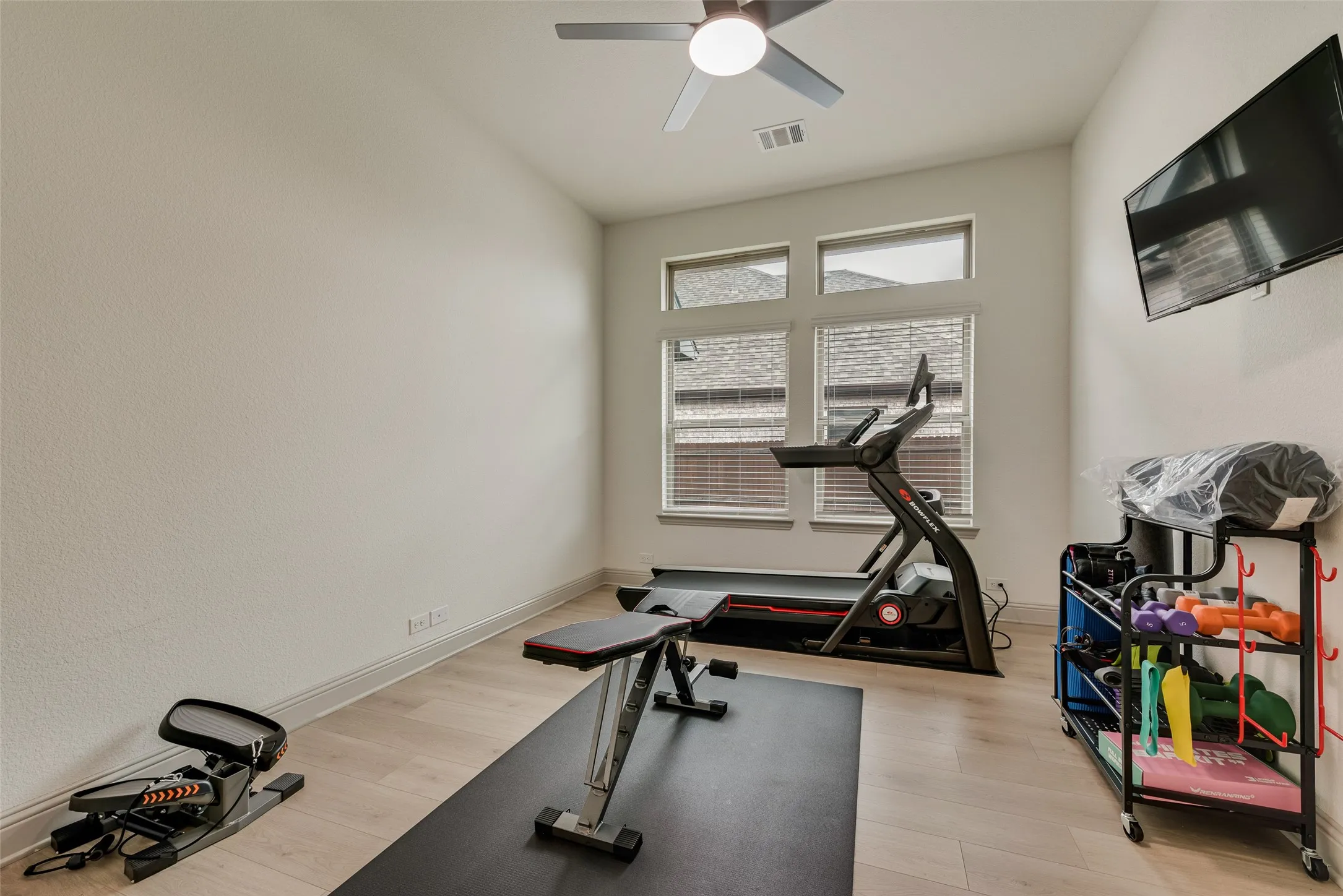 Study currently used as an exercise room, with wood-finish flooring, a ceiling fan, and windows with blinds