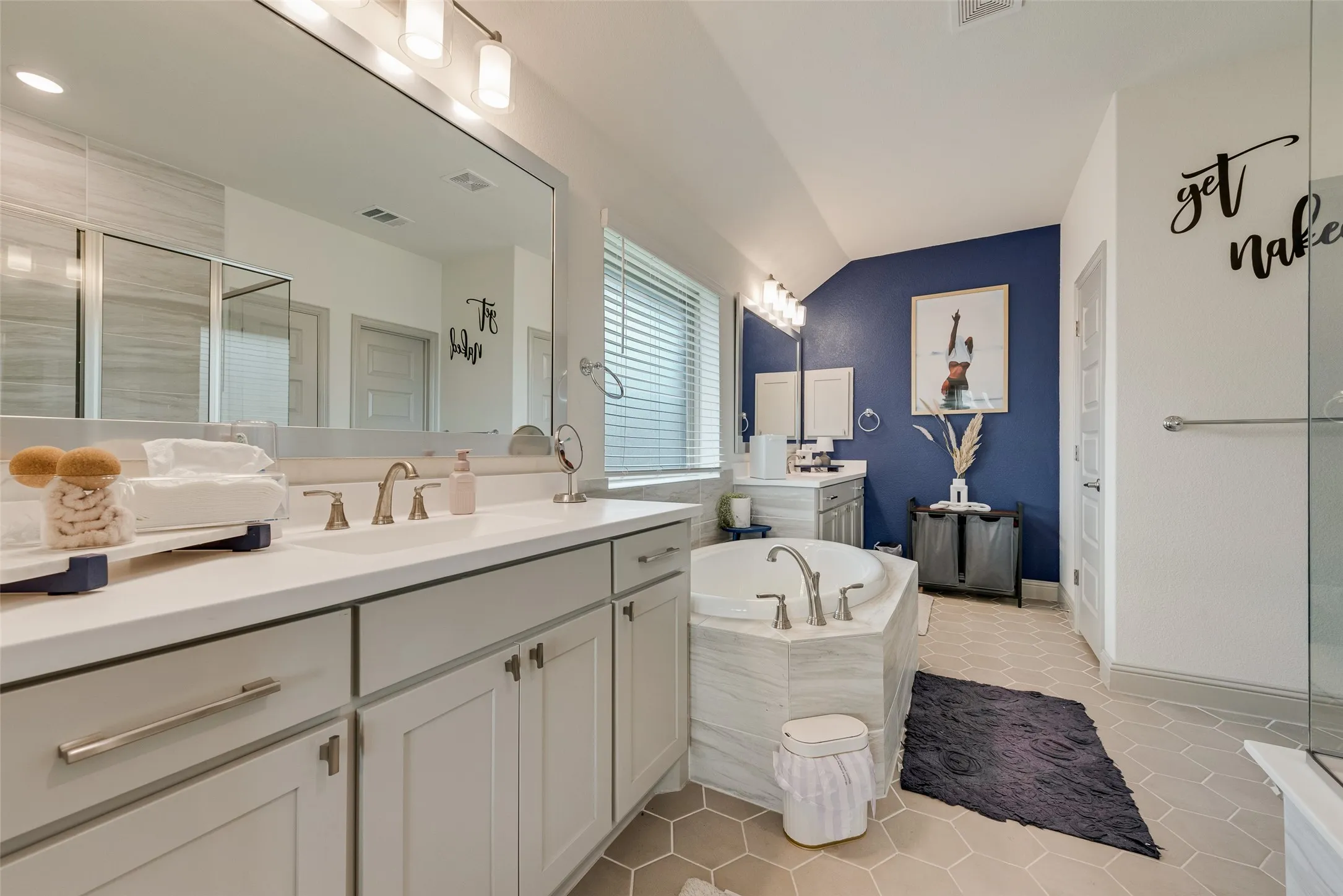Dual-sink vanity with light gray cabinetry and white countertops, alongside a soaking tub