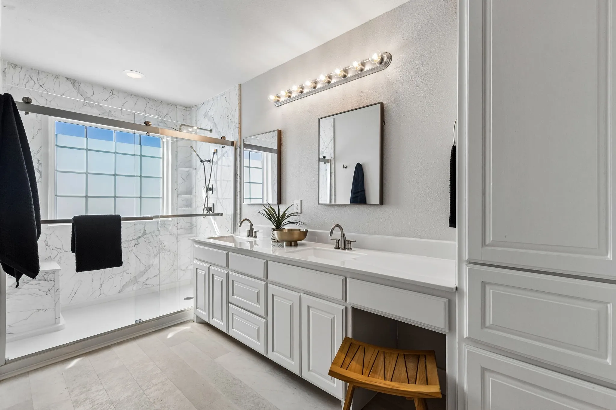 Large walk-in shower, dual vanity with integrated sinks and white countertops, complemented by white cabinetry and a built-in storage tower