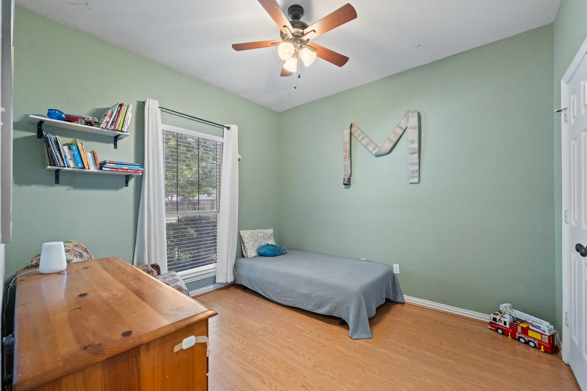 Recessed window with blinds and drapes, wood-finish flooring, ceiling fan with light fixture, built-in shelving
