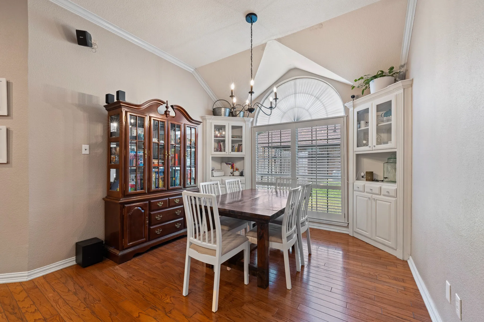 Vaulted ceiling with crown molding, wood-finish flooring, bay window with arched transom, and built-in cabinetry with glass display doors