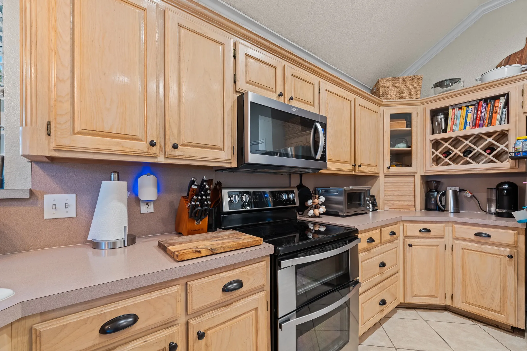 Kitchen featuring wood-finish cabinetry, stainless steel microwave, black electric range with double ovens, integrated wine rack, and tile flooring