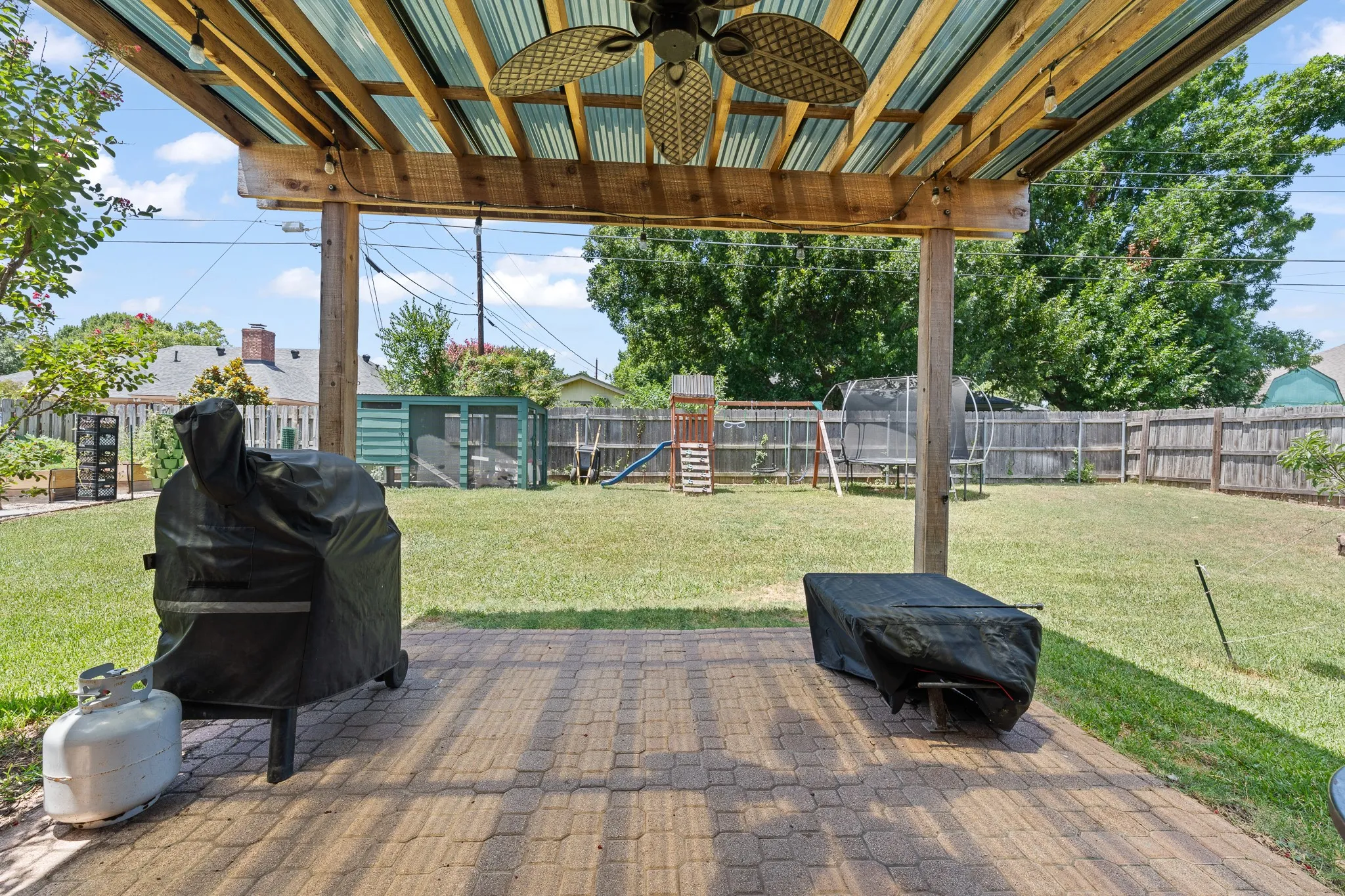 Covered outdoor patio with paver flooring, wood beam construction, and a ceiling fan