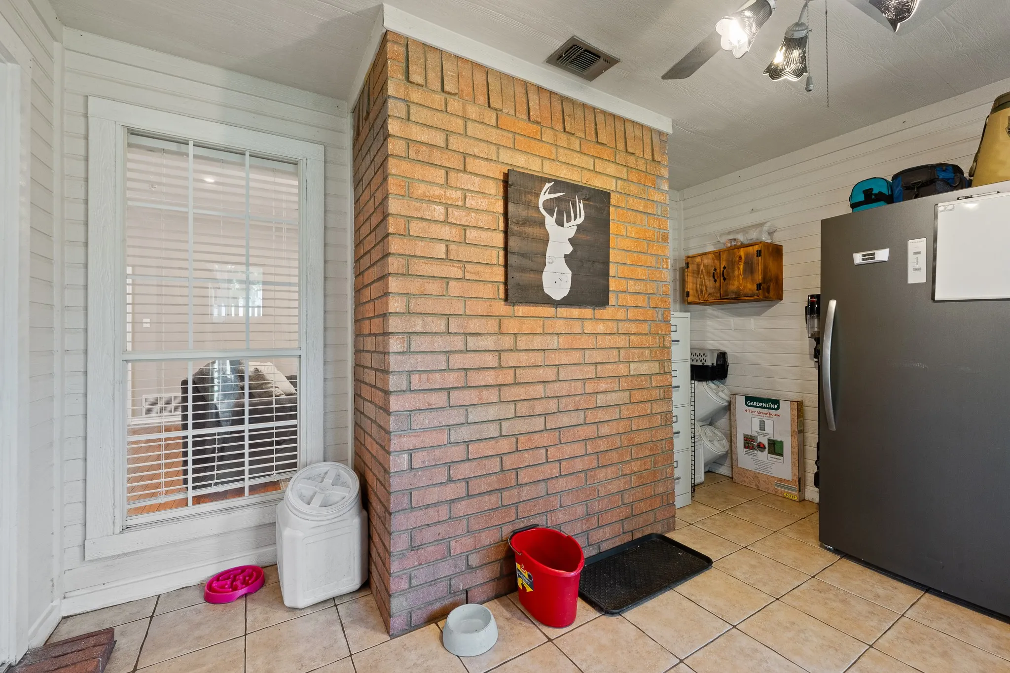 Brick column accenting the space, featuring tile flooring, a window with horizontal blinds, and shiplap wall paneling