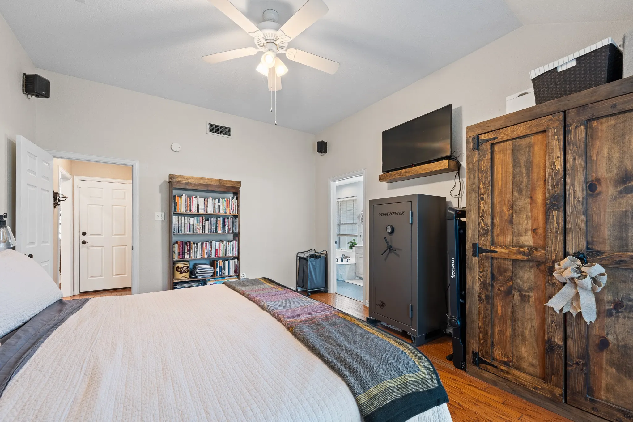Vaulted ceilings, wood-finish flooring, white ceiling fan with light fixture, built-in wooden bookshelf, and a large wooden armoire