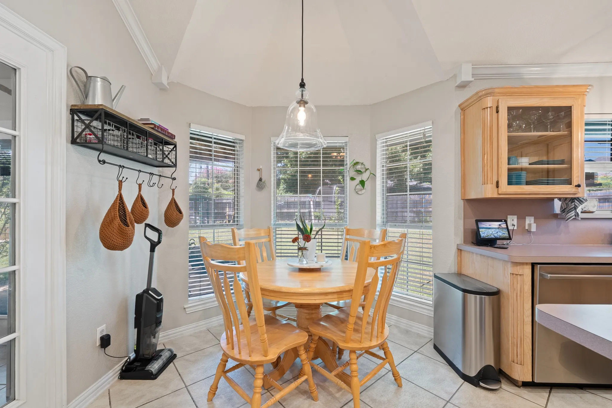 Angled dining area with tile flooring, multiple windows, and a glass-front upper cabinet