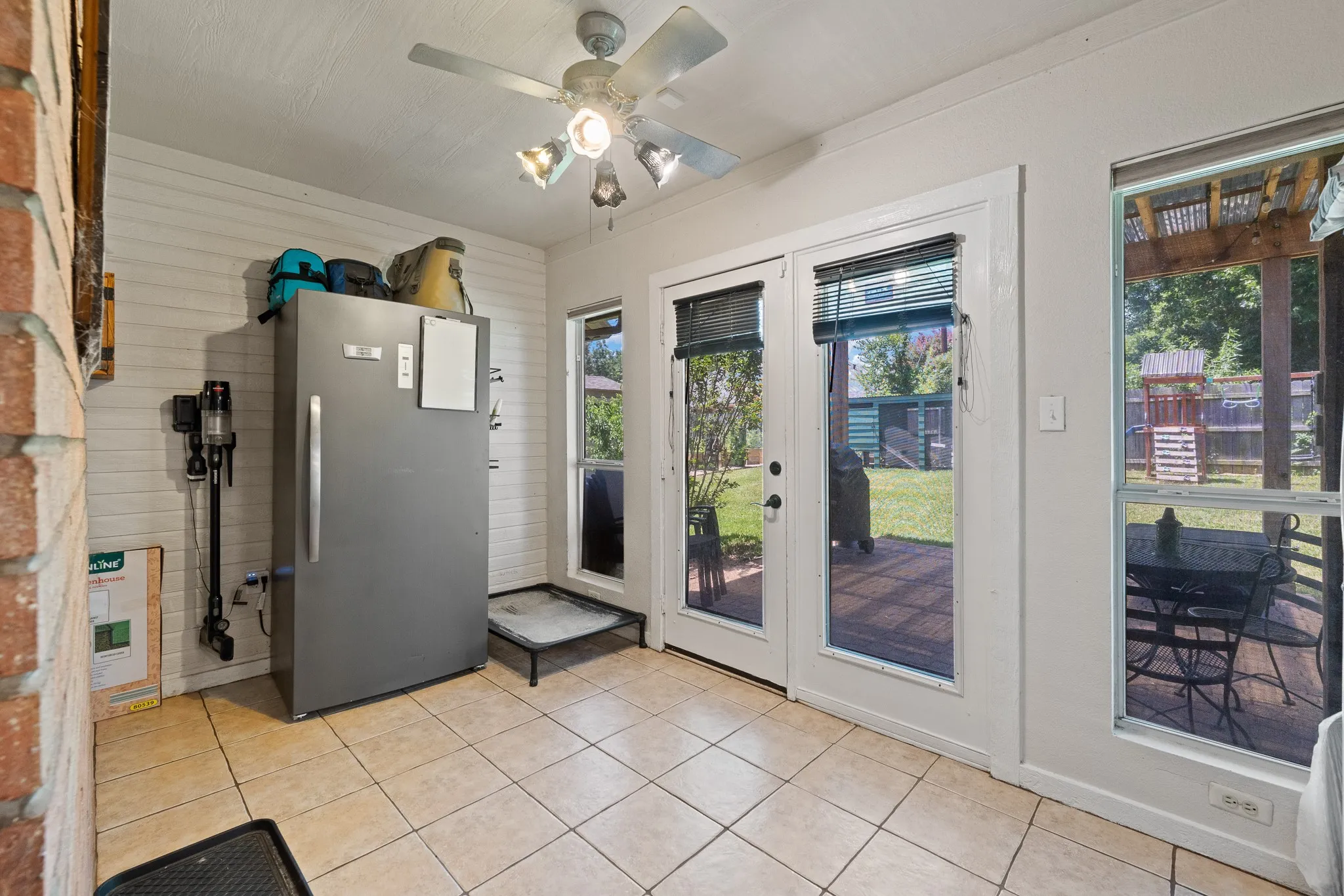 Tiled flooring, double patio doors, multiple windows, and a ceiling fan with integrated lighting