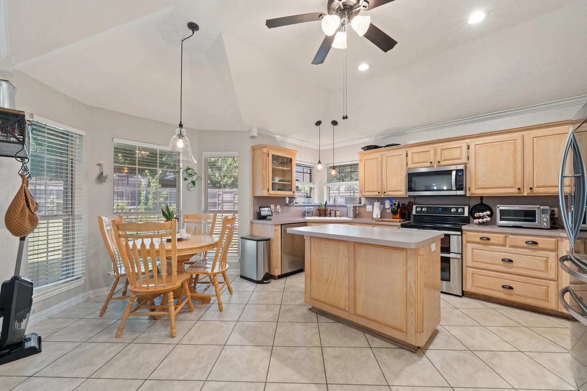 Kitchen featuring a central island, tile flooring, wood cabinetry, stainless steel appliances, and vaulted ceiling
