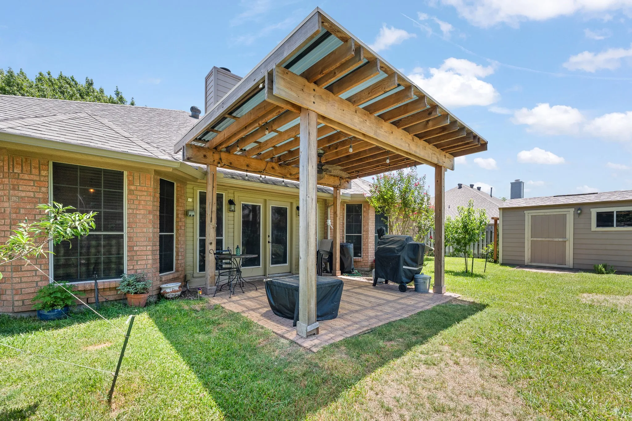 Expansive backyard featuring a wood pergola with a translucent roof, brick paver patio, brick exterior, and a detached storage shed