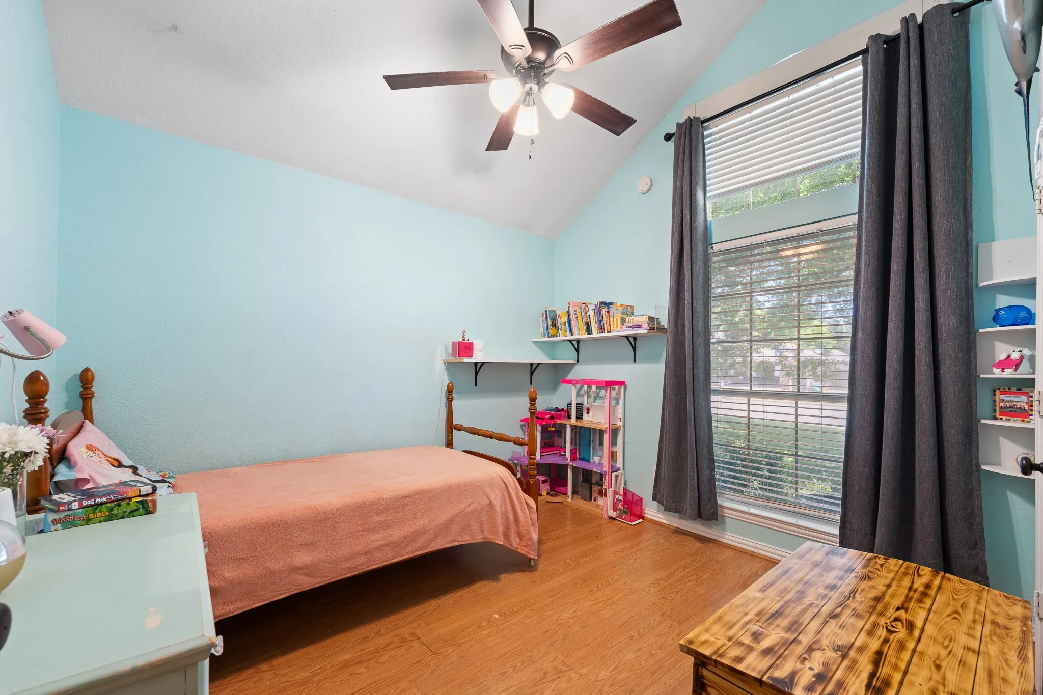 Vaulted ceiling with a ceiling fan, wood-finish flooring, built-in shelving, and a large window with blinds