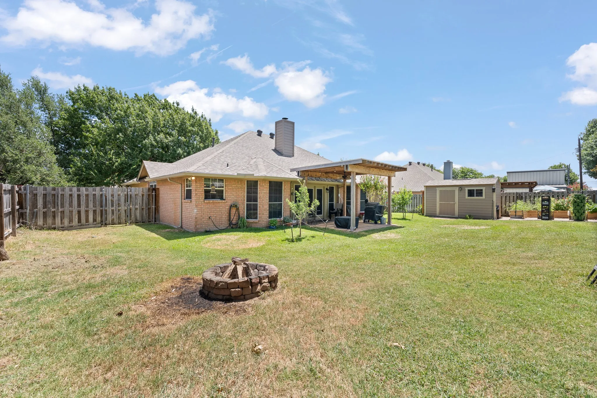 Expansive backyard featuring a stone-ringed fire pit, covered patio, privacy fencing, and a detached storage shed