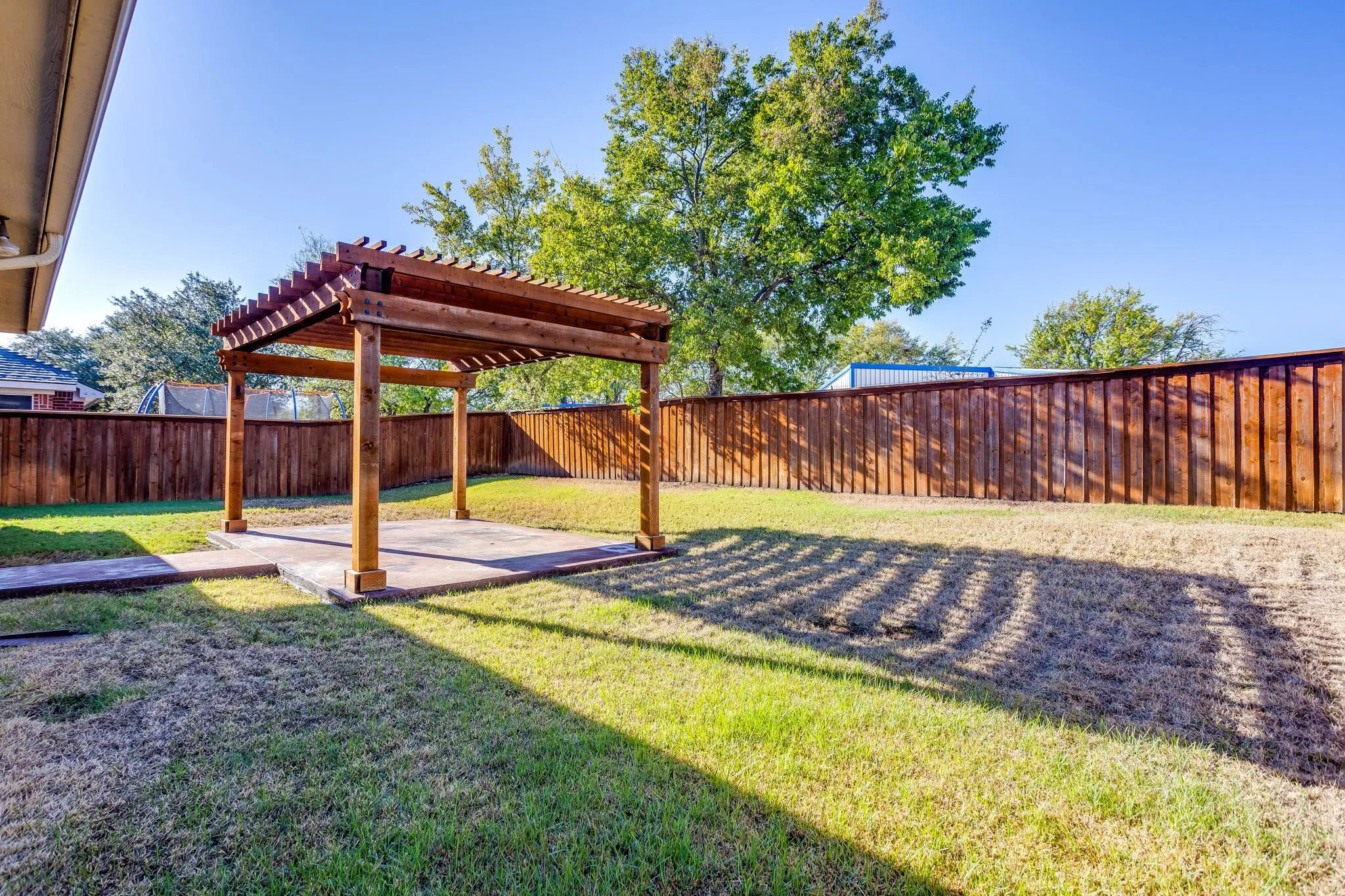 Expansive backyard featuring a wood pergola over a concrete patio and a wood privacy fence