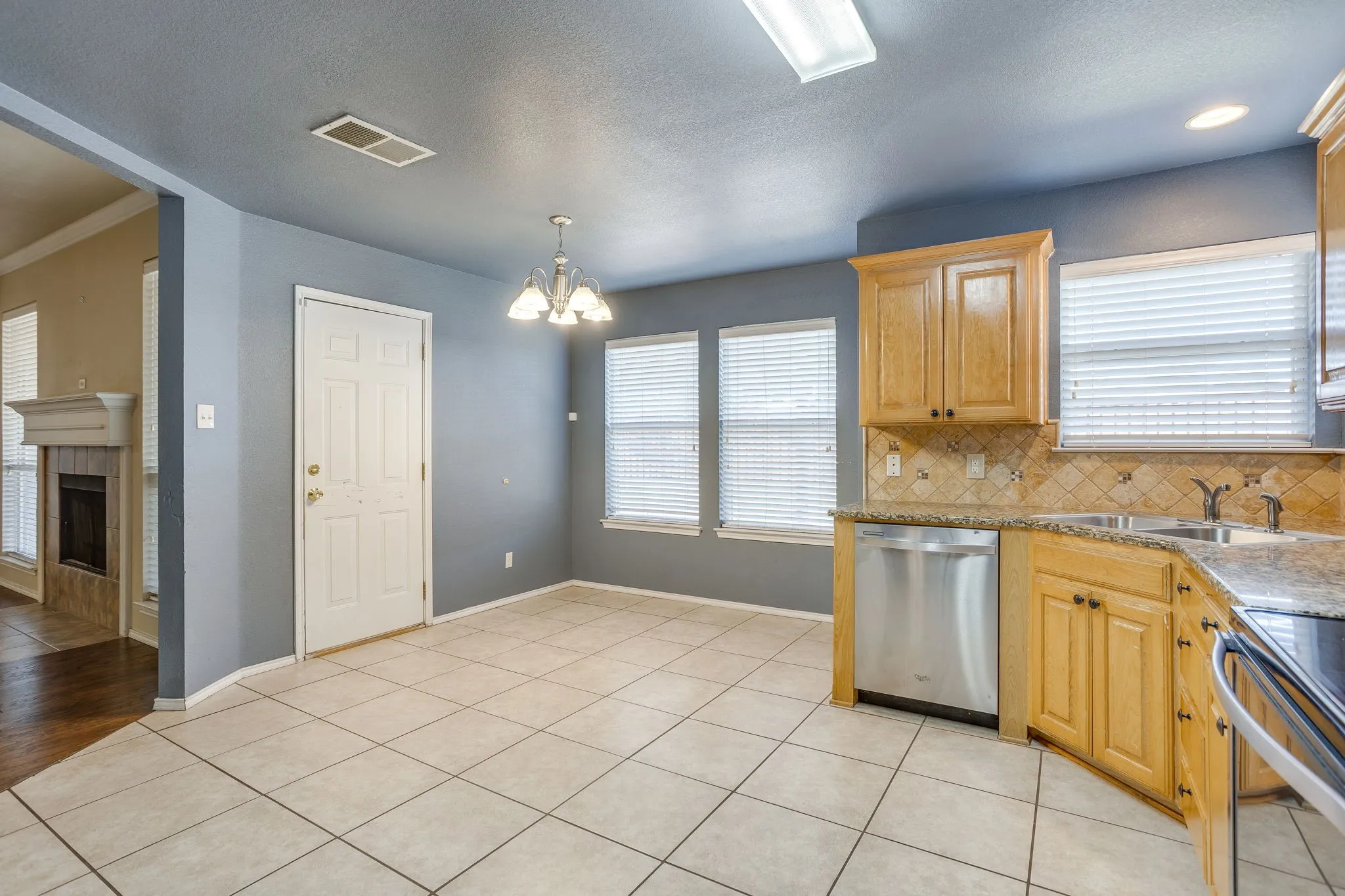 Kitchen with wood cabinetry, stainless steel dishwasher, tile backsplash, and granite countertops