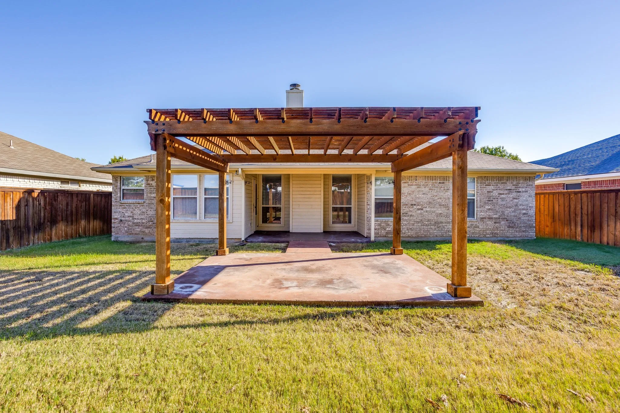 Expansive backyard featuring a stained concrete patio, wooden pergola, and a privacy fence