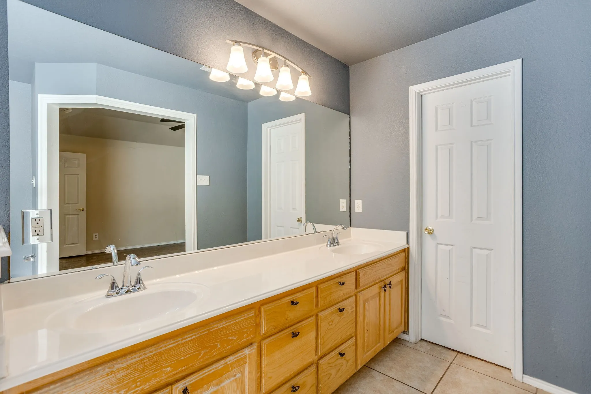 Dual vanity with integrated sinks, wood-finish cabinetry, chrome fixtures, and a multi-bulb light fixture