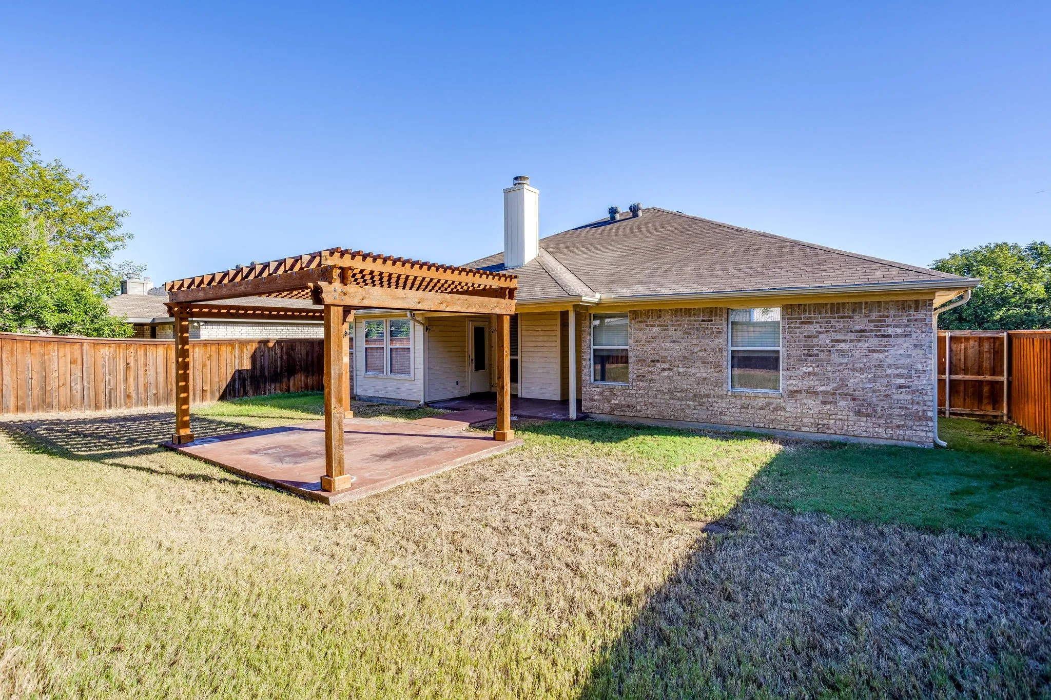 Expansive backyard featuring a wood pergola and concrete patio, brick exterior, and wood privacy fencing