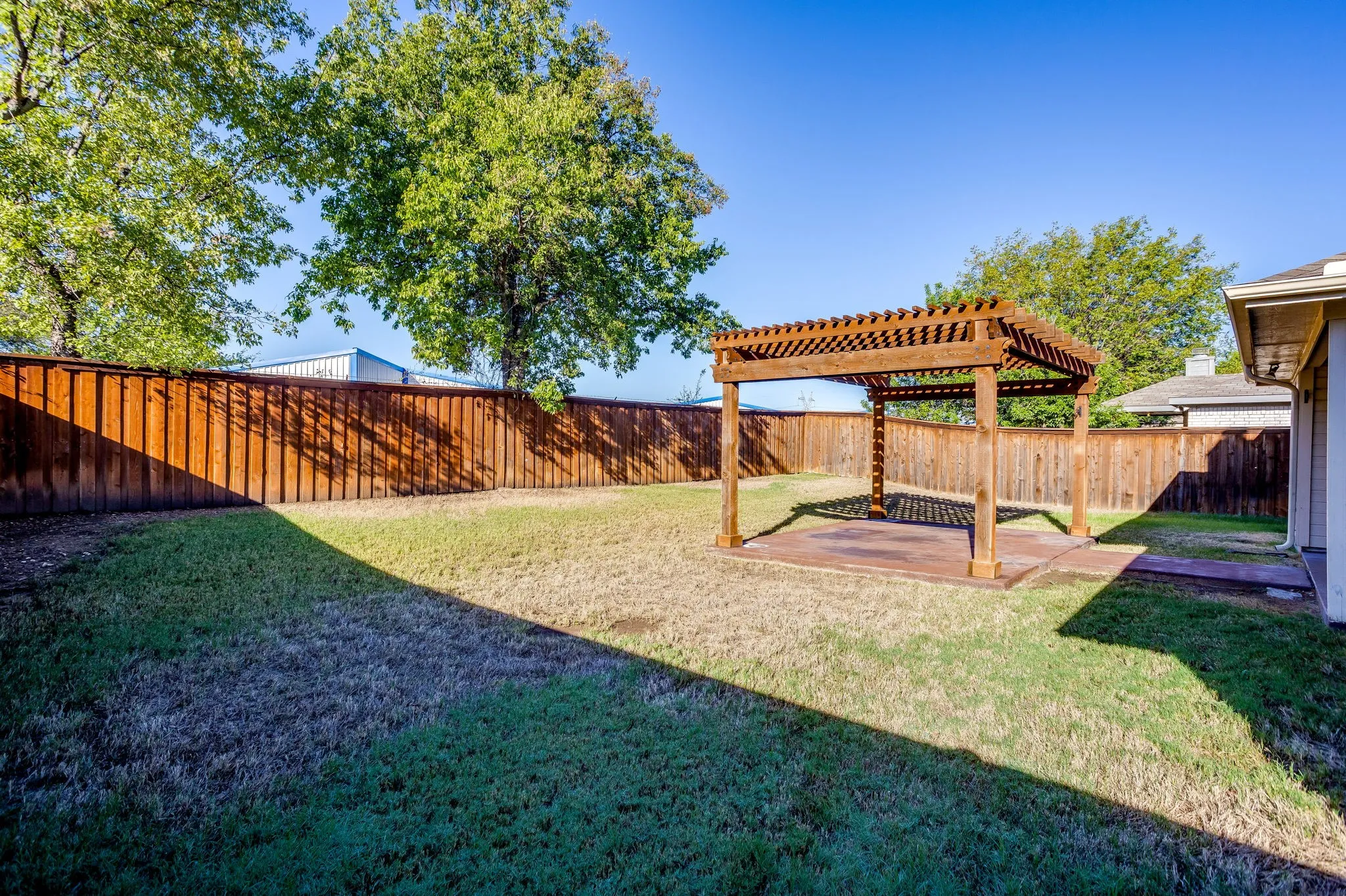 Spacious backyard featuring a wood pergola over a concrete patio and a wood privacy fence