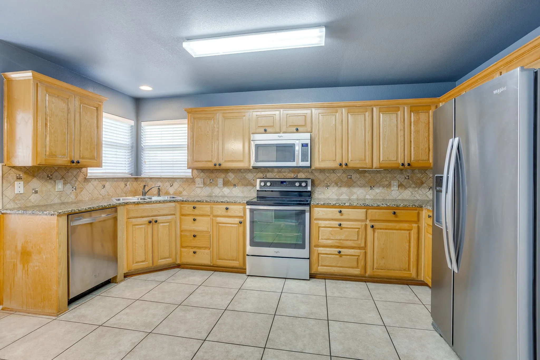 Kitchen featuring wood cabinetry, stainless steel appliances, granite countertops, and tiled flooring