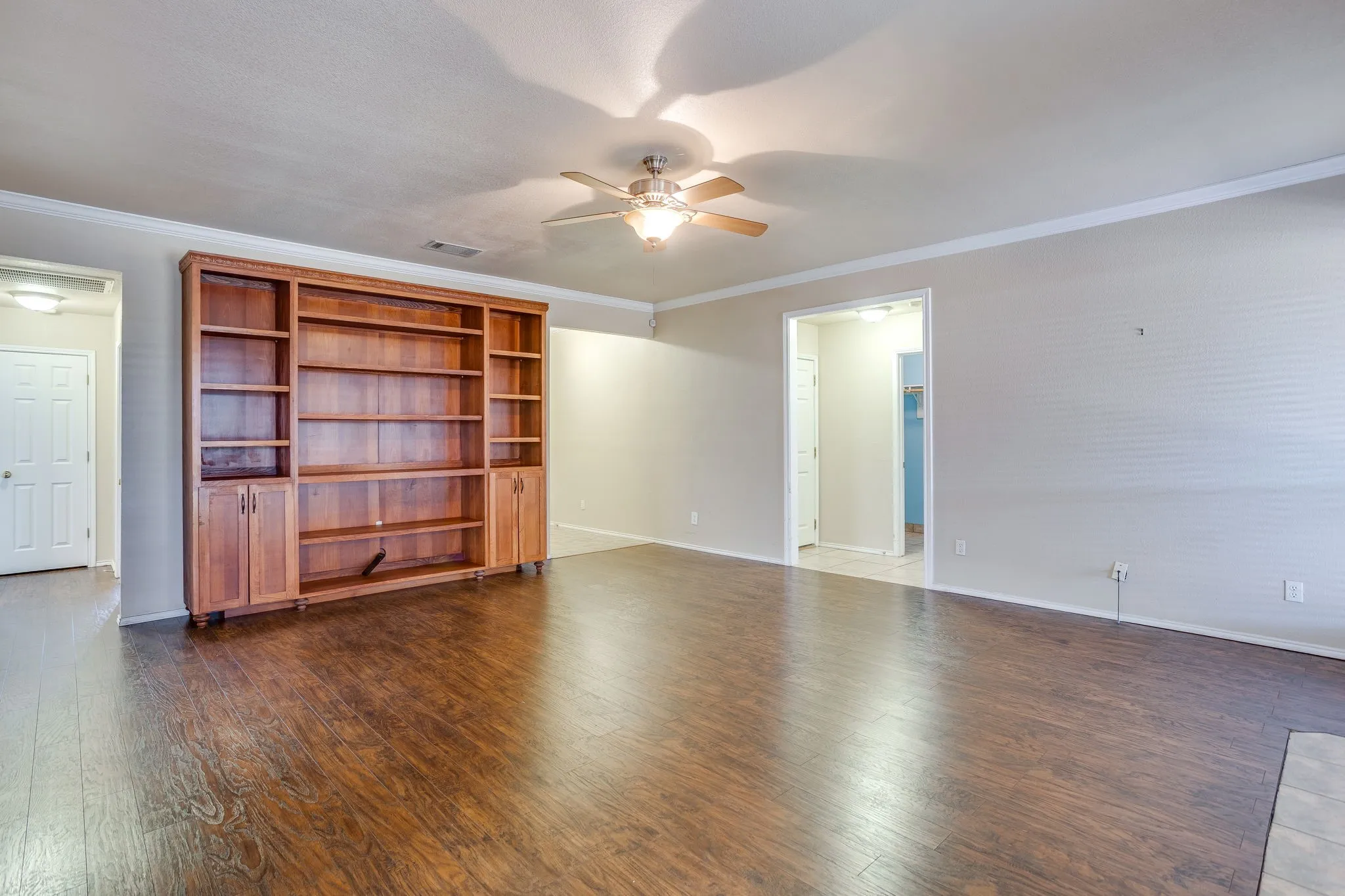 Wood-finish flooring, built-in shelving with cabinetry, crown molding, and ceiling fan with lighting