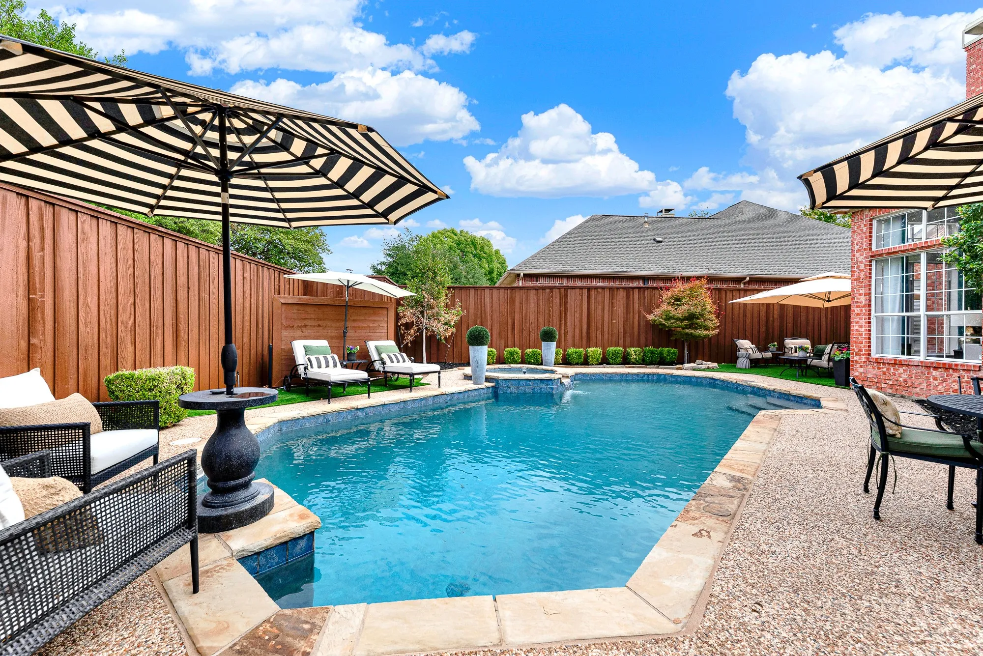 A privacy fence stained in 2026 encloses this private oasis around sparkling blue pool waters. Lounge comfortably poolside on warm sunny afternoons with a cool drink in hand.