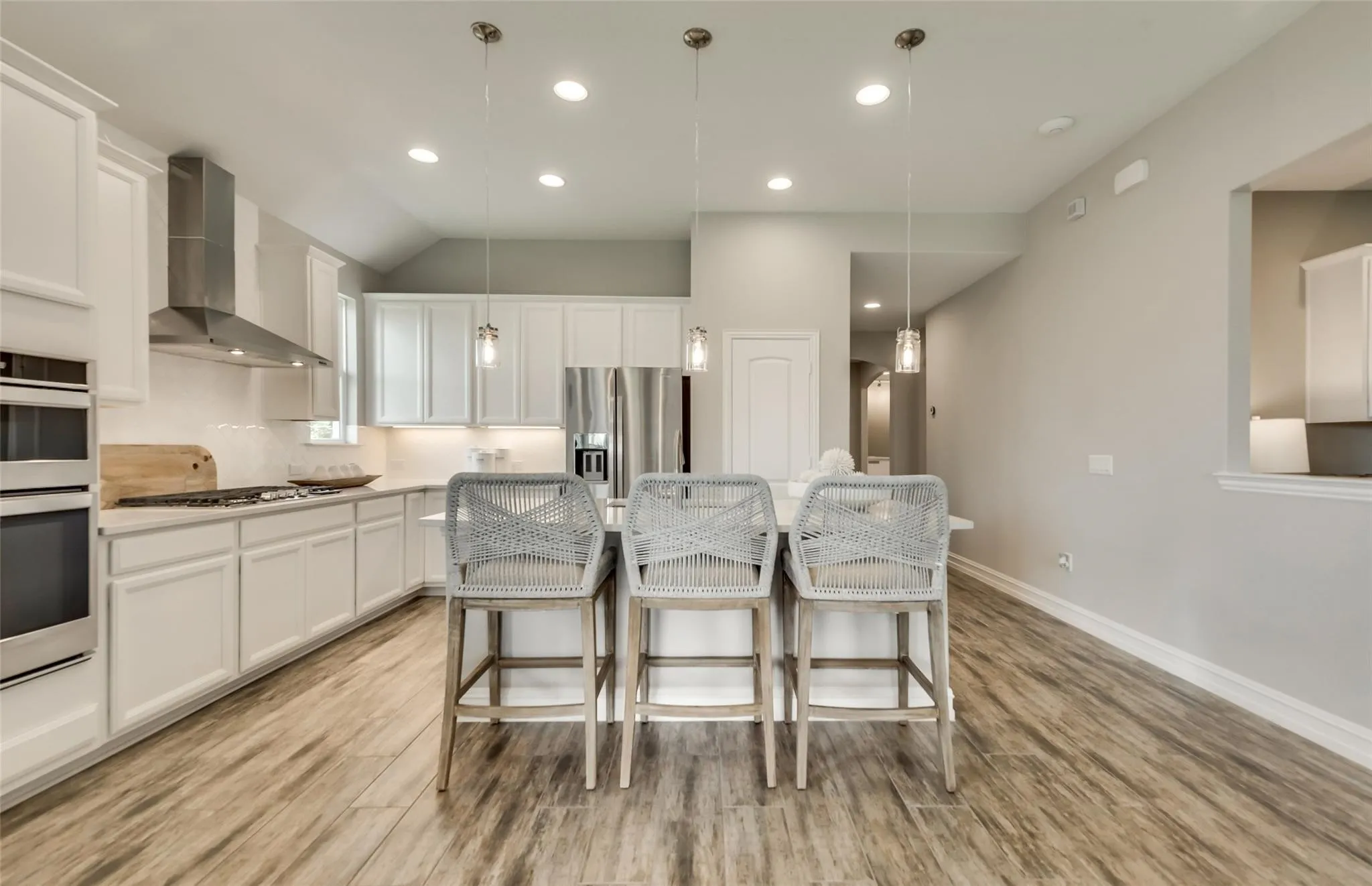 White cabinetry, stainless steel appliances, wood-finish flooring, recessed lighting, and a kitchen island with pendant lighting