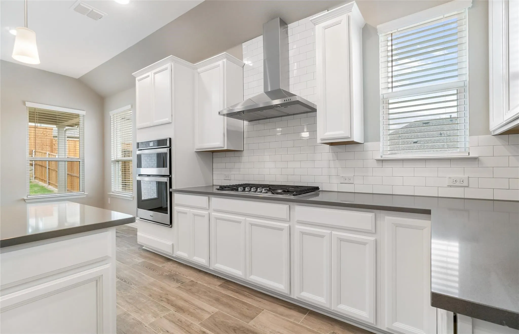 Kitchen featuring shaker-style white cabinetry, dark countertops, a subway tile backsplash, stainless steel double ovens, and wood-finish flooring