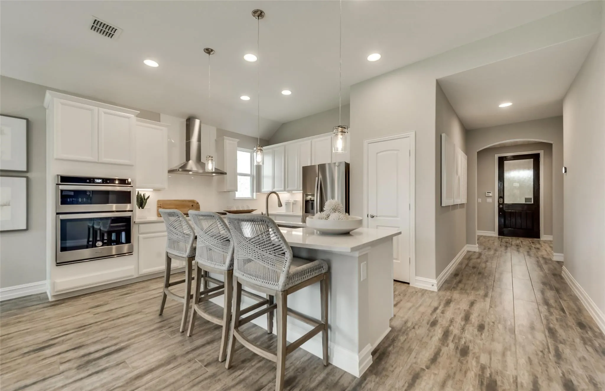 Kitchen featuring white cabinetry, stainless steel appliances, wood-finish flooring, and an island with pendant lighting