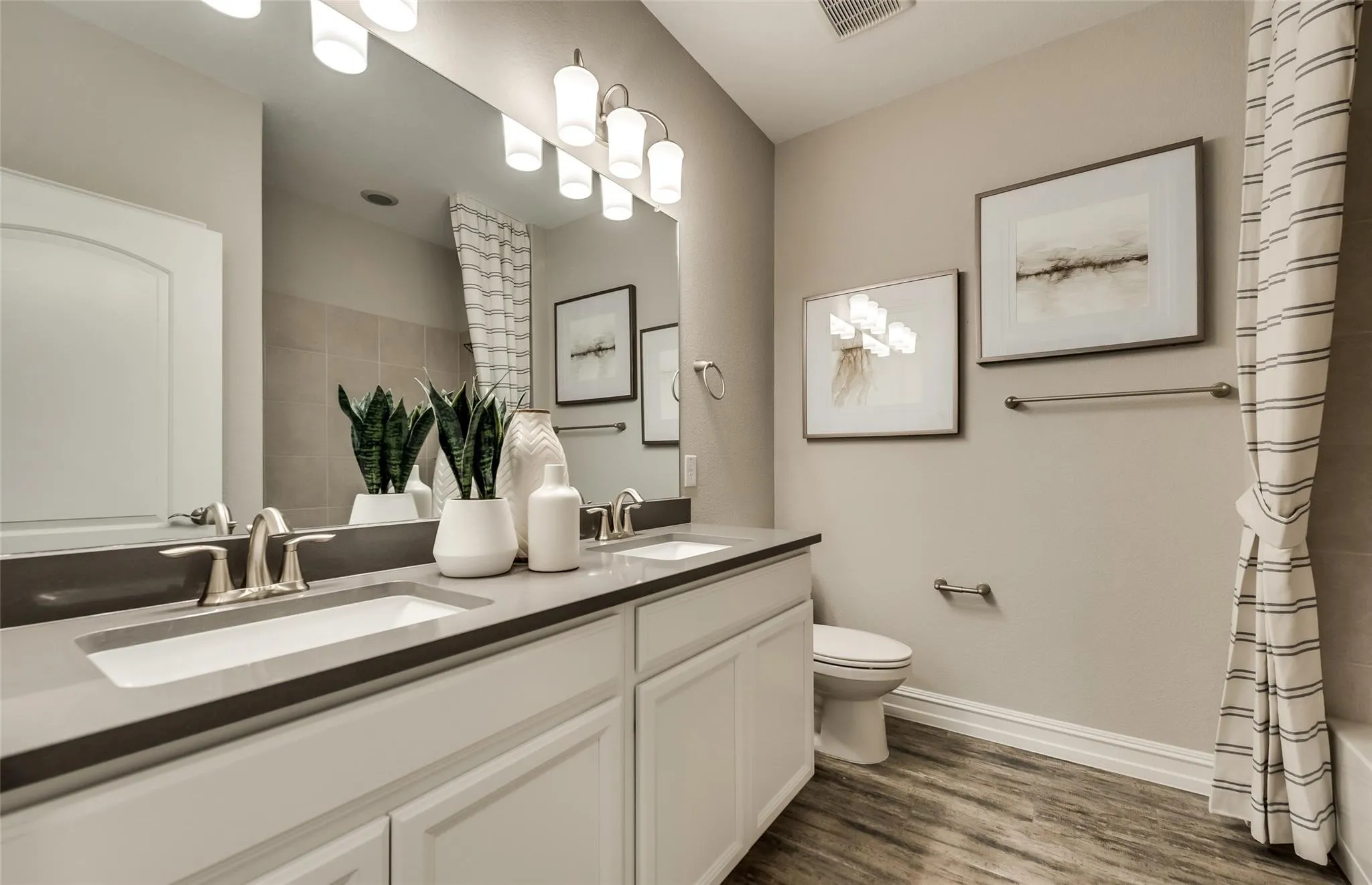 Dual vanity with undermount sinks and dark countertops, wood-finish flooring, and a large wall mirror