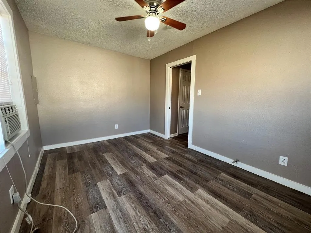 Wood-finish flooring, ceiling fan with integrated lighting, neutral wall paint, white trim, and a window-mounted air conditioning unit