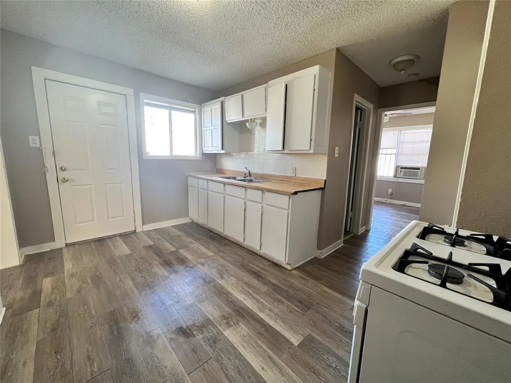 Kitchen featuring wood-finish flooring, white cabinetry, a window for natural light, and a built-in range
