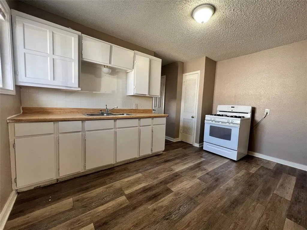 Kitchen featuring wood-finish flooring, white cabinetry, a white gas range, and a dual-basin sink with a wood-finish countertop