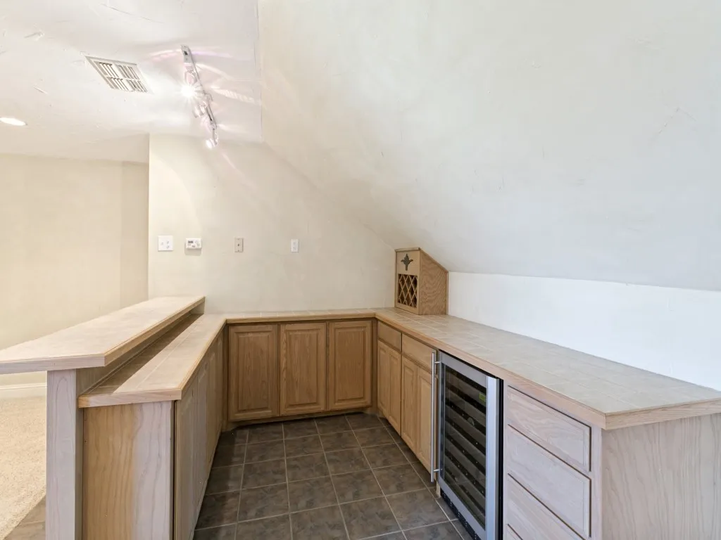 Built-in bar featuring wood cabinetry, tile flooring, light-toned countertops, and a built-in beverage refrigerator