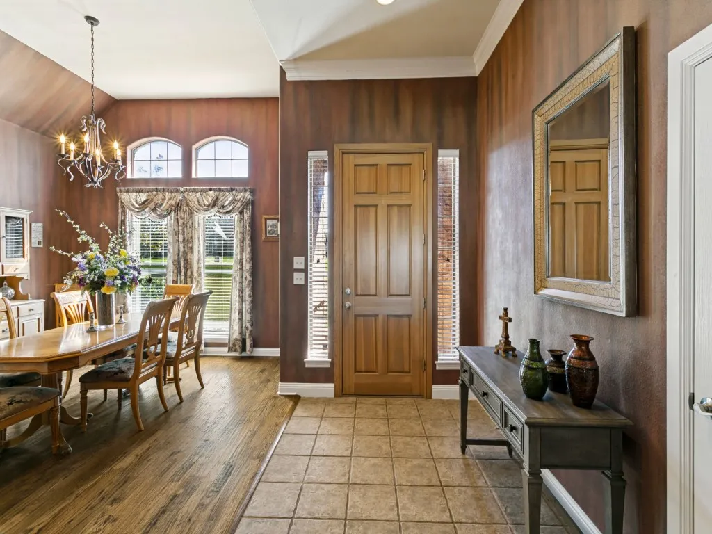 Wood-finish flooring, tiled entry, arched transom windows, and a chandelier with decorative scrollwork