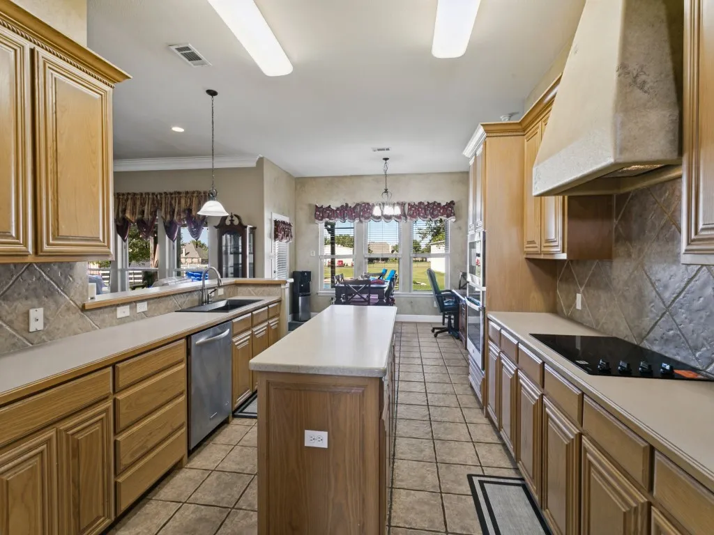 Kitchen featuring wood cabinetry, stone-look countertops, a built-in cooktop, tile flooring, and a stone-clad range hood