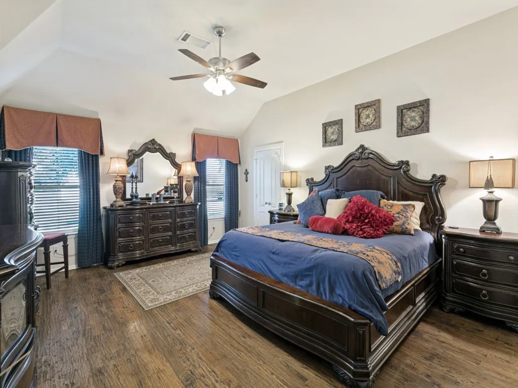 Vaulted ceiling featuring a ceiling fan, wood-finish flooring, and multiple windows with blinds