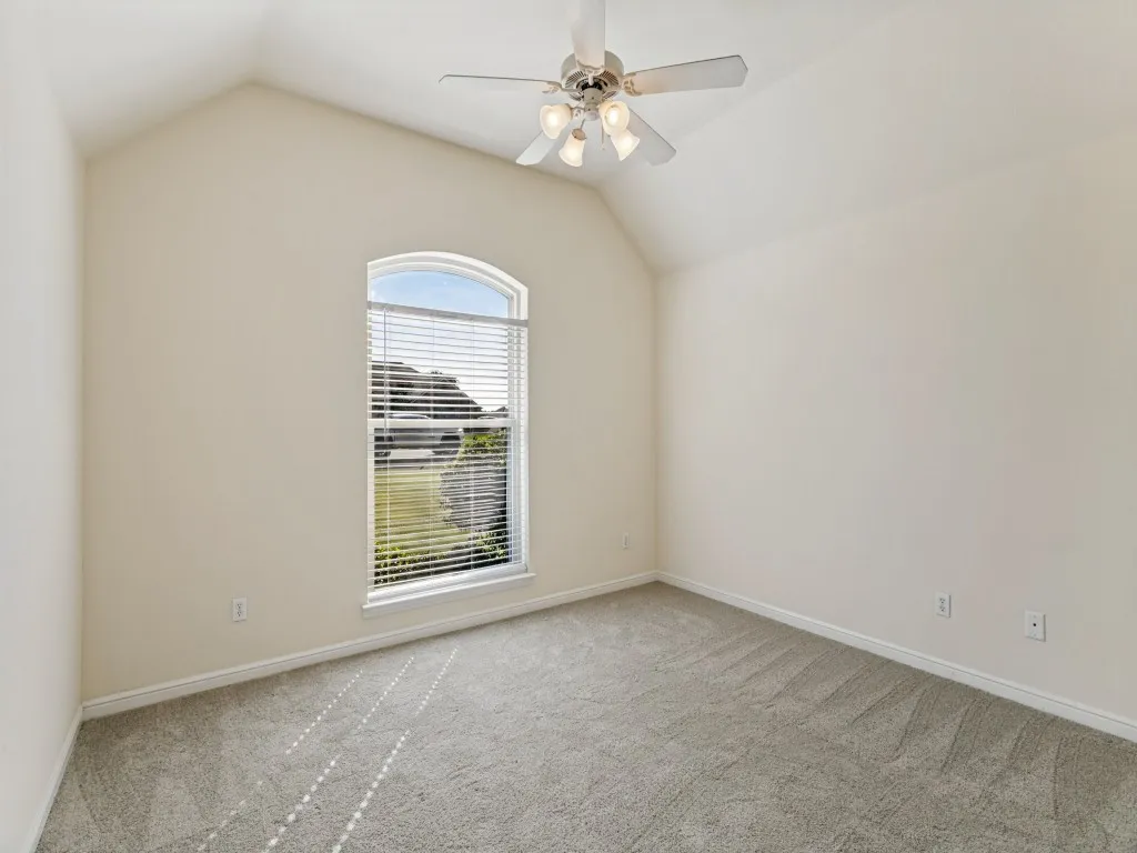 Vaulted ceiling featuring a ceiling fan with light kit, arched window with horizontal blinds, and carpeting